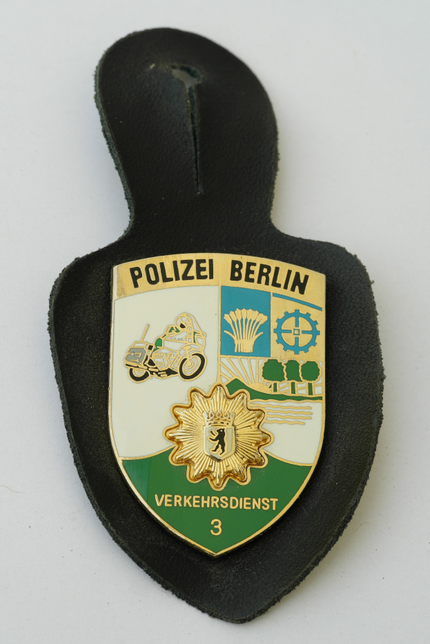 Ein Polizeischild mit den Wörtern "Polizei Berlin" darauf, das ein blaues Schild mit einem weißen Stern in der Mitte zeigt, umgeben von einem weißen Rand, auf einer Oberfläche platziert.