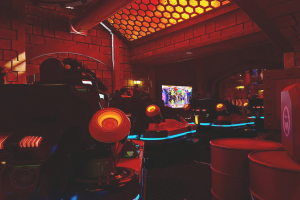 Ein hell erleuchteter Arcade-Raum voller verschiedener Videospielautomaten, Bildschirme und andere Gegenstände, einschließlich einer sichtbaren Rohrleitung an der Wand.