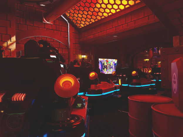 Ein hell erleuchteter Arcade-Raum voller verschiedener Videospielautomaten, Bildschirme und andere Gegenstände, einschließlich einer sichtbaren Rohrleitung an der Wand.