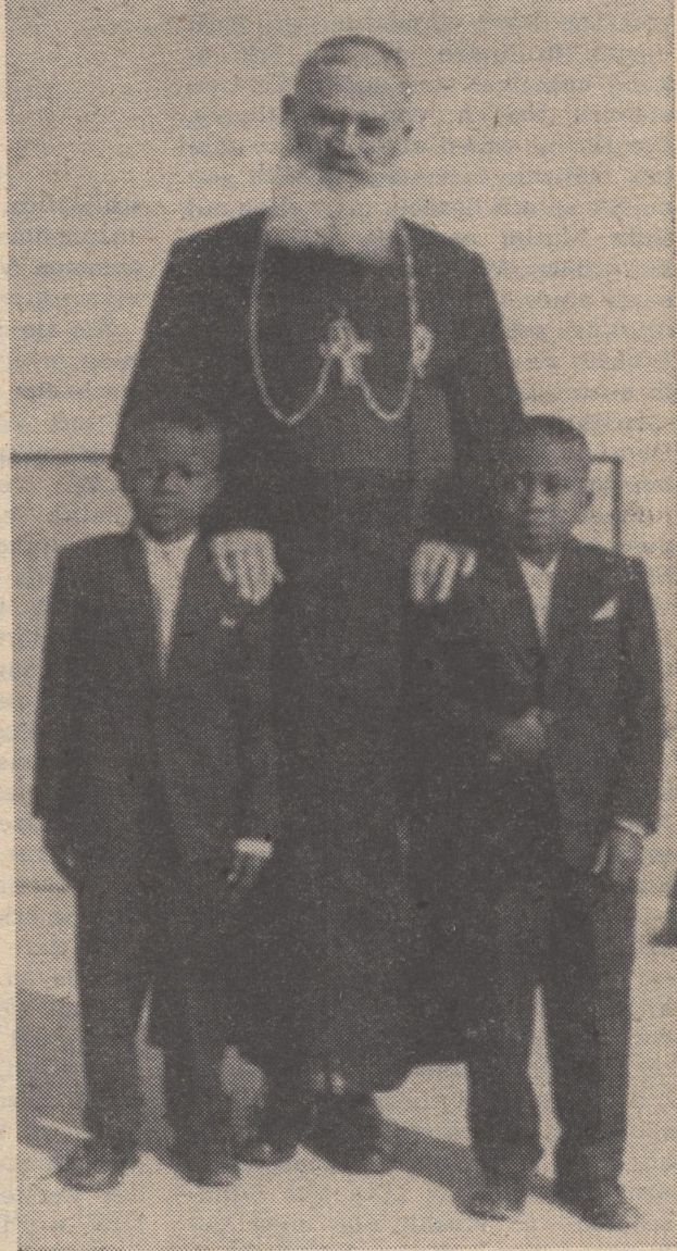Ein Schwarz-Weiß-Foto eines Mannes, der neben zwei Jungen in Blazern und Krawatten steht, mit Text unten, der darauf hinweist, dass er ihr Vater ist.