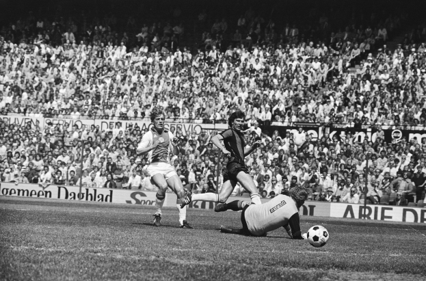 Schwarzes und weißes Foto von Männern, die auf einem Feld Füßball spielen, mit Zuschauern im Hintergrund und einer Bundesliga 1978-79 Ajax 1-1 Hannover 96-Fahne.