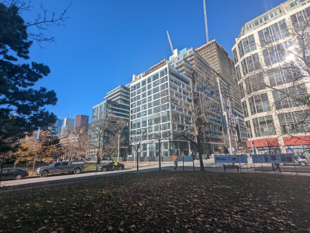 Eine Stadtstraße in Toronto mit hohen Gebäuden, Fahrzeugen, Fußgängern, Bäumen und trockenen Blättern auf dem Boden unter einem sichtbaren Himmel.