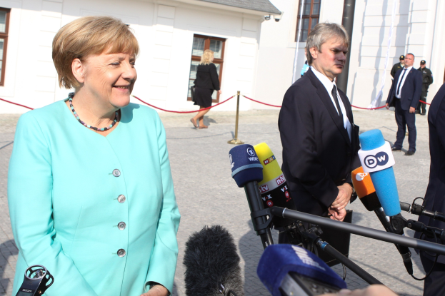 Bundeskanzlerin Angela Merkel spricht mit Reportern vor einem Gebäude mit Fenstern und einem bewölkten Himmel.
